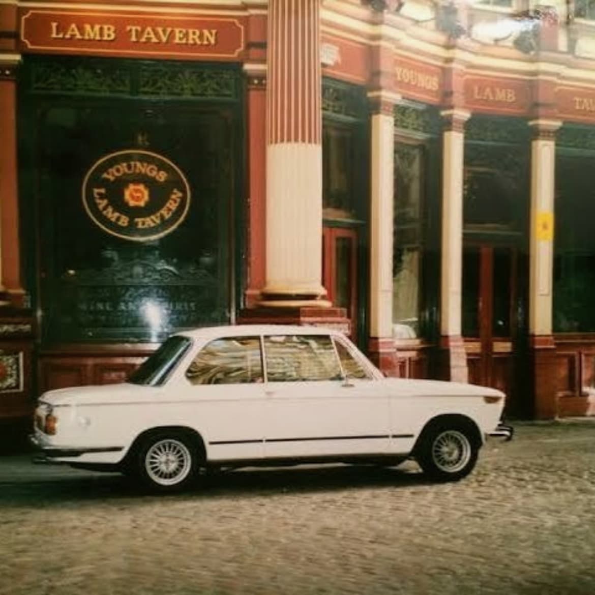 A white BMW parked on cobbles outside the Lamb Tavern, its windows lit behind.